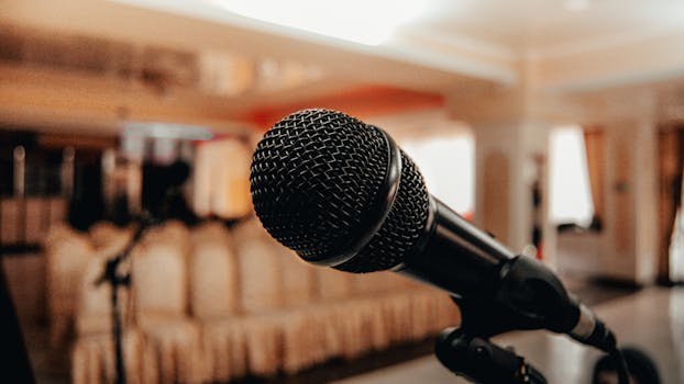 Closeup of black modern microphone on stand placed in spacious meeting room with chairs